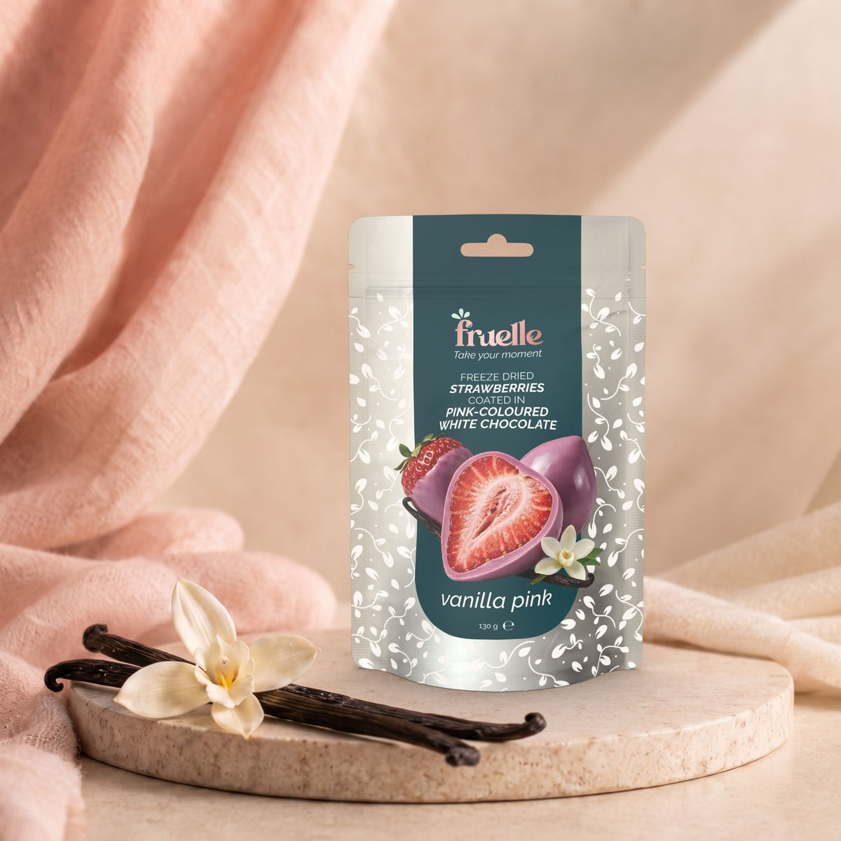 Fruelle Vanilla Pink met gevriesdroogde aardbeien omhuld met roze witte chocolade, naast vanillestokjes en een vanillebloem